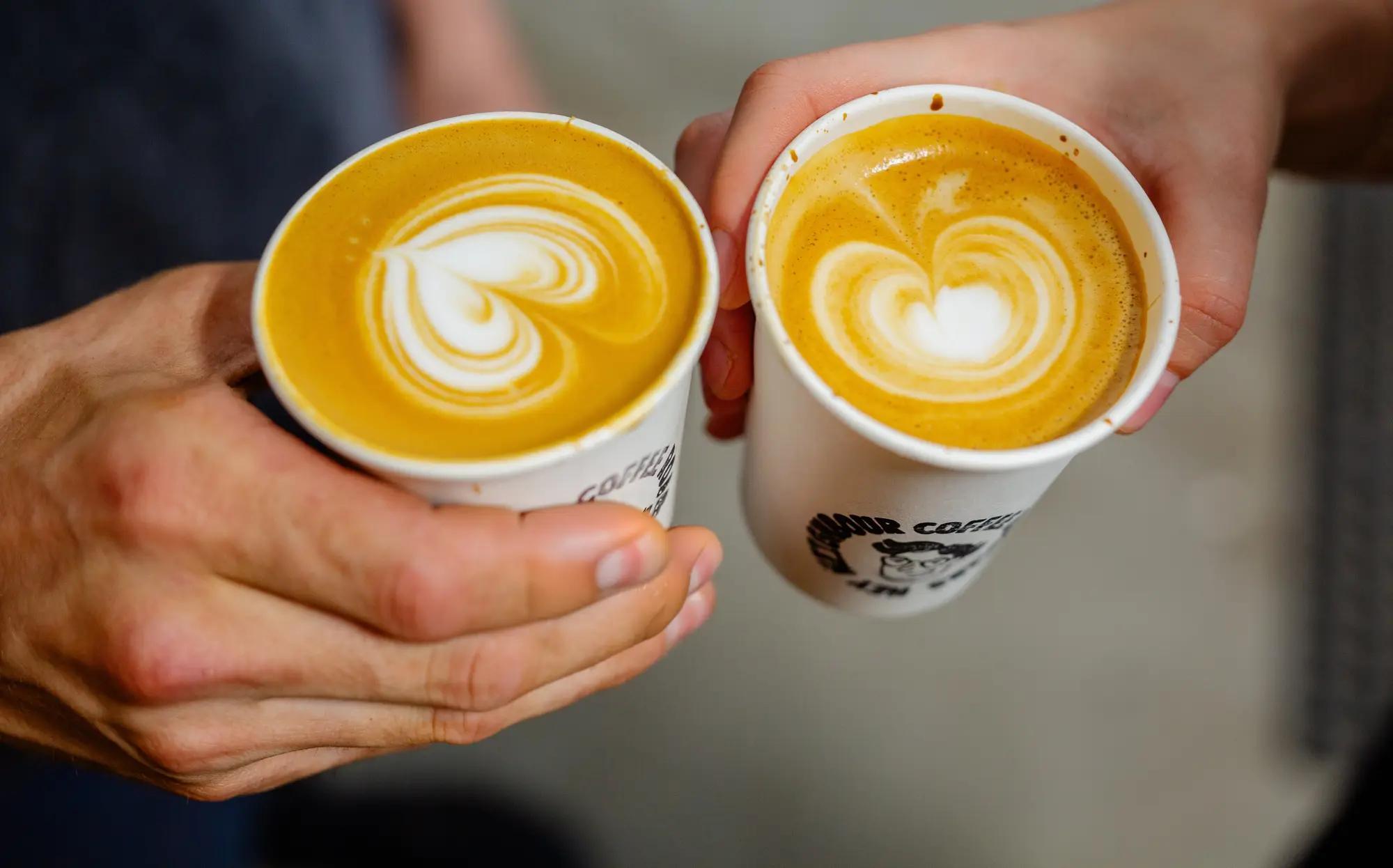 Two Hey Neighbour cups of coffee with latte art, held together in a cheers